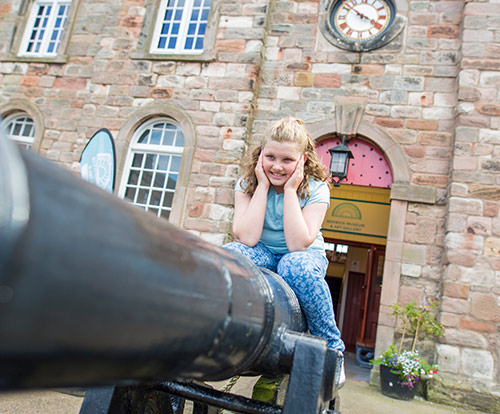 A child sits astride a cannon. The entrance to the old museum is behind her