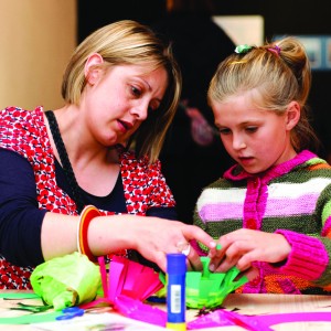 An adult and child take part in crafts. There is lots of colourful cardboard and a glue stick