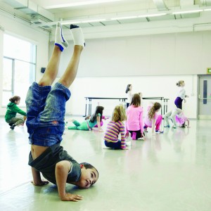 A child in a dance studio with their head, hands and chest near the floor and their legs in the air