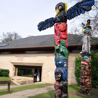 A colourful totem pole with the modern exterior of the Captain Cook Birthplace Museum in the background