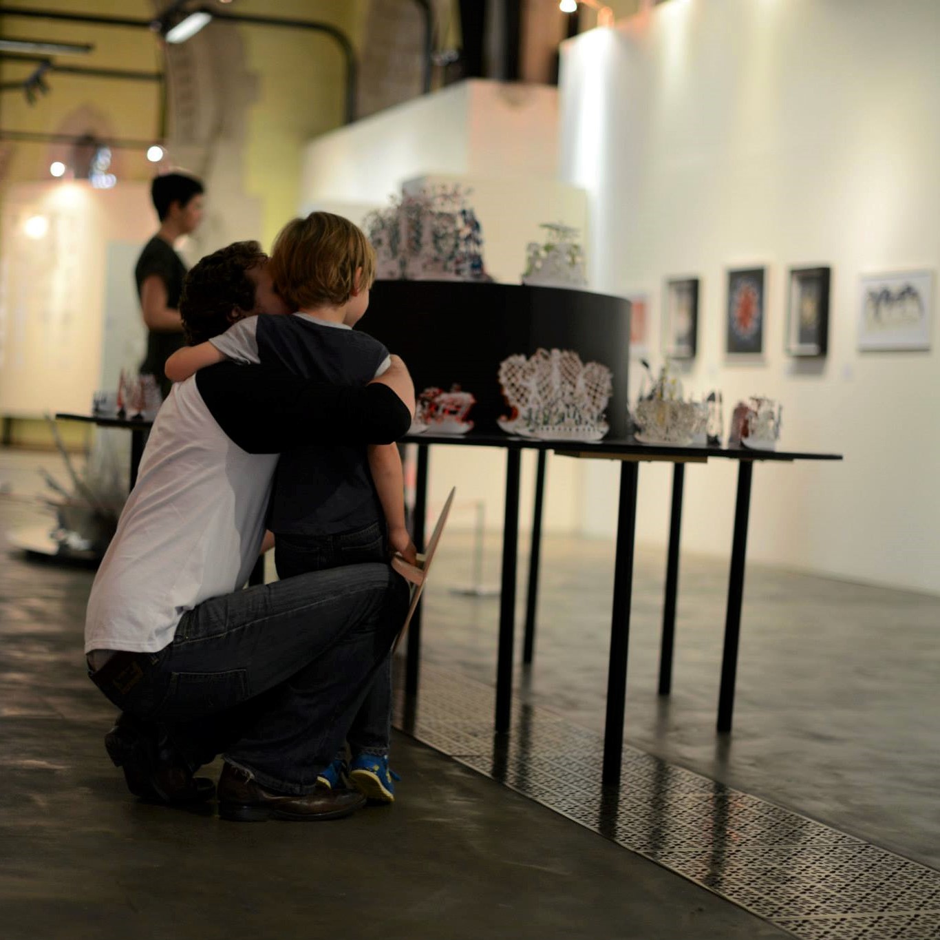 An adult and child with their arms around each other look at exhibits on a table